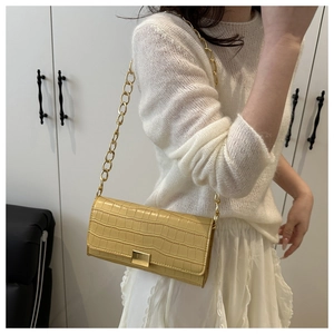 Détail d'un sac à main jaune pâle à texture crocodile avec bandoulière chaîne dorée
