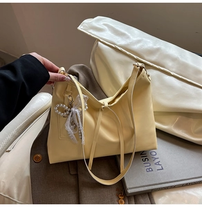 Detail of light yellow leather tote bag with elegant pearl lace bow pendant and metal charm