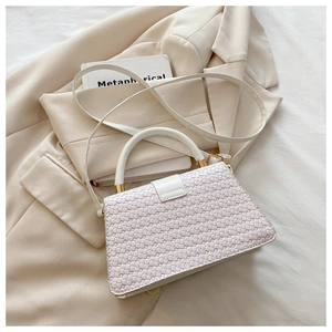 Détail de la texture en cuir tressé crème et ferrures dorées d'un petit sac à bandoulière
