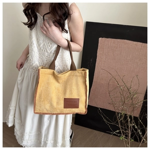 Detail of yellow corduroy tote bag with brown straps and leather fashion label