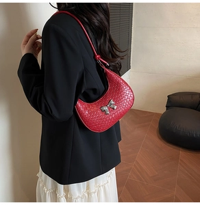 Detail of red crescent shoulder bag with woven leather texture and silver bow charm
