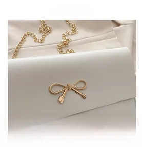 Detailed close-up of white leather bag with golden bow clasp and refined metal chain strap