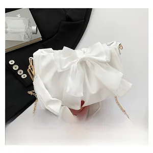 Detail of white fashion shoulder bag featuring large bow and gold chain strap accents