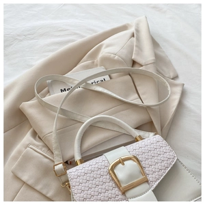 Détail d'un sac à main tressé crème avec grande boucle dorée sur fond de blazer chic