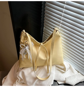 Detail of soft pale yellow tote bag with a white lace pearl bow charm and matte texture