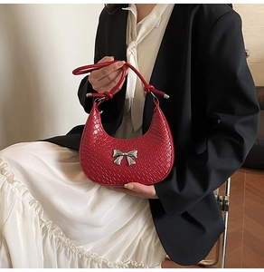 Detail of red crocodile pattern crescent bag with silver bow ornament and knot strap