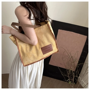 Detail of yellow corduroy tote bag featuring dark brown handles and a leather brand patch