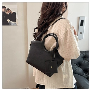 Detail of black tote bag with embossed texture and small square pouch pendant on model