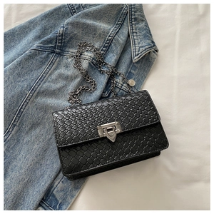 Close-up of black woven leather texture and silver shield-shaped rotary lock on flap bag
