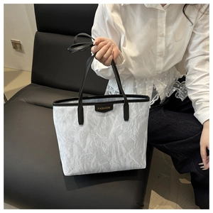 Detail of white wrinkled tote bag with black trim and gold FASHION label