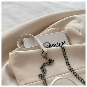 Détail du sac à main en cuir blanc avec chaîne en métal gris sur blazer beige