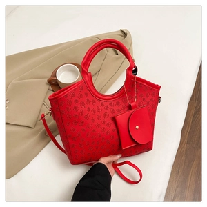 Detail of red tote bag with clover pattern, featuring dual handles and a small charm pouch