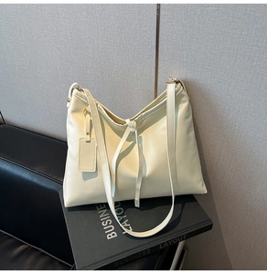 Detail der cremeweißen Kunstledertasche mit Zierknoten und goldenen Beschlägen