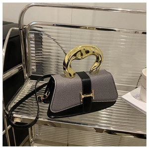 Close-up of grey fabric and black leather crossbody bag with bold gold metal handle