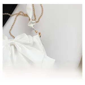 Detail of white satin shoulder bag featuring a large bow and elegant gold chain strap