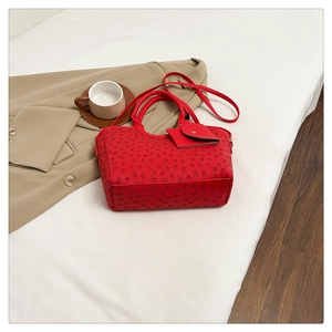 Detail of red floral tote bag featuring a small hanging pouch and adjustable strap on a bed