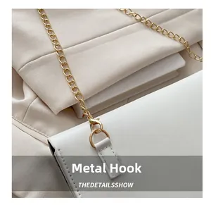 Close-up of golden metal lobster clasp and chain strap on white leather shoulder bag