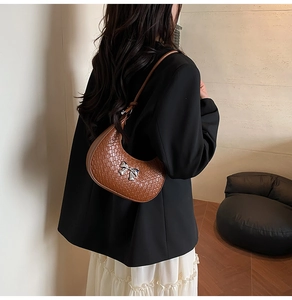 Detail of a brown crescent bag with crocodile texture and silver metal bow ornament