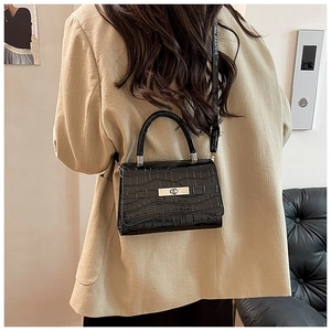 Detail of black crocodile texture handbag with silver metal buckle on beige blazer