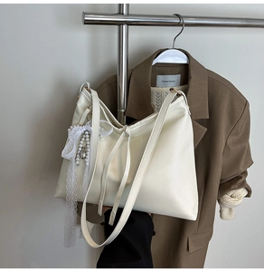Detail of cream white PU leather tote bag with pearl and lace bow pendant accessory