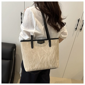 Close-up of beige tote bag with pleated texture and black contrast shoulder straps on model