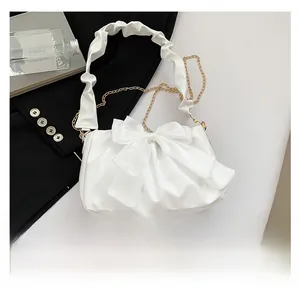 Detail of white pleated handbag featuring a large bow and gold chain strap accents