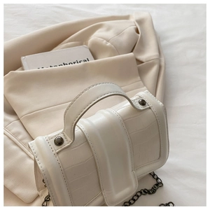 Détail d'un sac à main blanc motif crocodile avec chaîne en métal et poignée solide