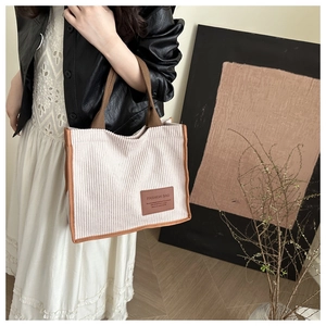 Detail of light beige corduroy tote bag featuring brown piping and fashion logo label