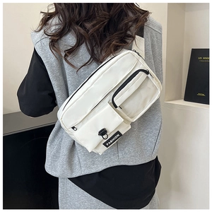 Détail du sac bandoulière en toile blanche avec design multi-poches et étiquette mode