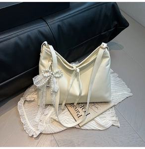 Detail of cream leather shoulder bag featuring a pearl lace bow charm and heart pendant