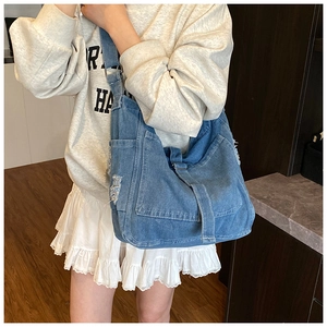 Fashionable large capacity blue distressed denim crossbody bag worn by female model