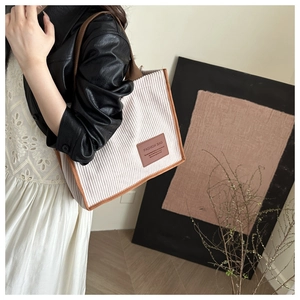 Detail of beige corduroy tote bag with brown trim and fashion tag on a female model
