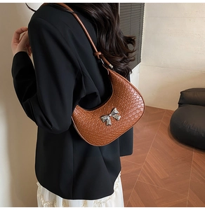Detail of brown woven crescent bag with silver bow charm worn by a model in black blazer