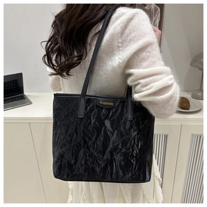 Detail of black wrinkled texture tote bag with golden fashion lettering on shoulder