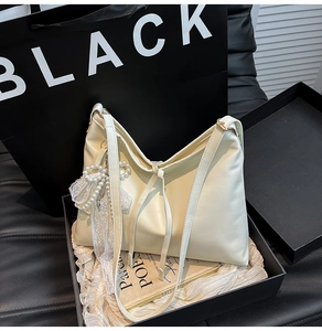 Detail of creamy PU leather tote bag featuring pearl bow and lace charm in a black gift box