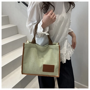 Detail of light green corduroy tote bag featuring brown leather patch and handles