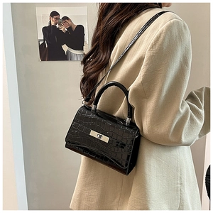 Detail of black crocodile texture bag with silver buckle worn over a beige blazer
