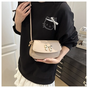 Détail du fermoir en forme de nœud doré sur un petit sac à bandoulière beige