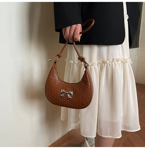 Detail of crocodile pattern hobo bag featuring a silver metal bow and knotted shoulder strap