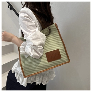 Detail view of light green corduroy tote bag with brown leather trim and fashion patch