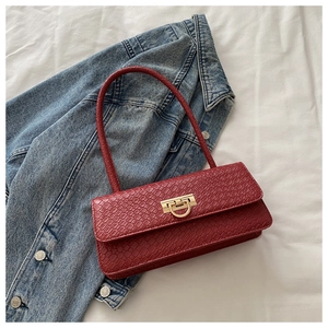 Detail of red crocodile texture handbag with golden horseshoe buckle on denim background
