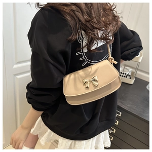 Détail du sac beige avec nœud doré et bandoulière nouée porté par un modèle