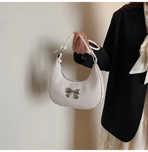 Detail of white crescent bag featuring woven texture and silver bow accent held by a model