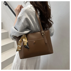 Dettaglio di una borsa tote marrone con cuciture bianche e sciarpa a fiori sulle scale