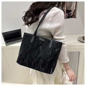 Detail of minimalist black tote bag featuring crinkled texture and gold metal fashion plate