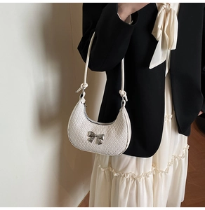 Close-up of white woven crescent bag with silver bow buckle and knotted shoulder strap