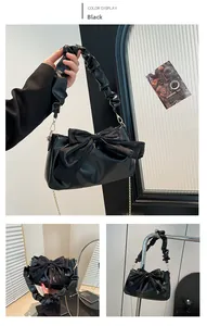 Detail of black faux leather handbag featuring a large bow and ruched handle design
