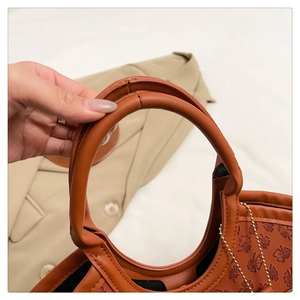 Detail of caramel leather tote bag with embossed leaf patterns and gold metal ball chain