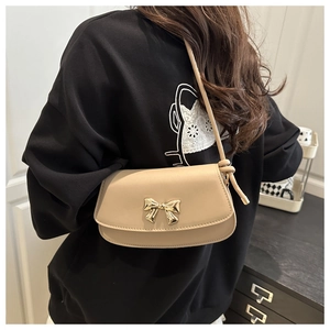 Détail du sac bandoulière beige avec un nœud en métal doré et une bandoulière à nœuds décoratifs