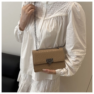 Close-up of woven texture handbag with metal chain strap and twist lock on model shoulder
